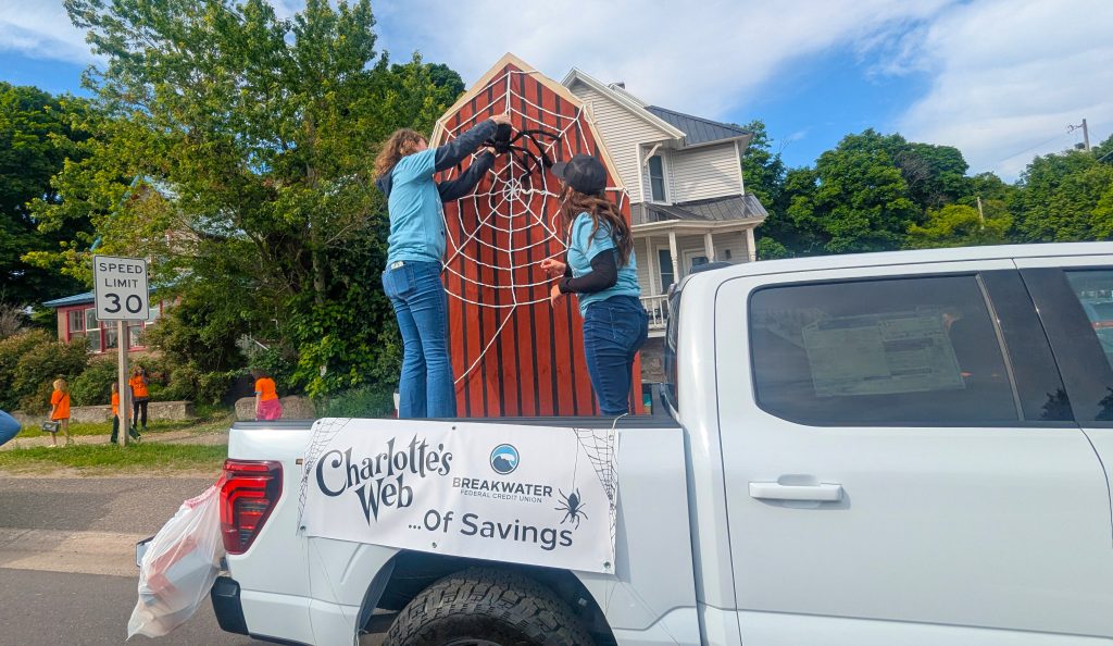 Staff pin web onto barn cutout sitting in truck bed to create Charlotte's Web of Savings.