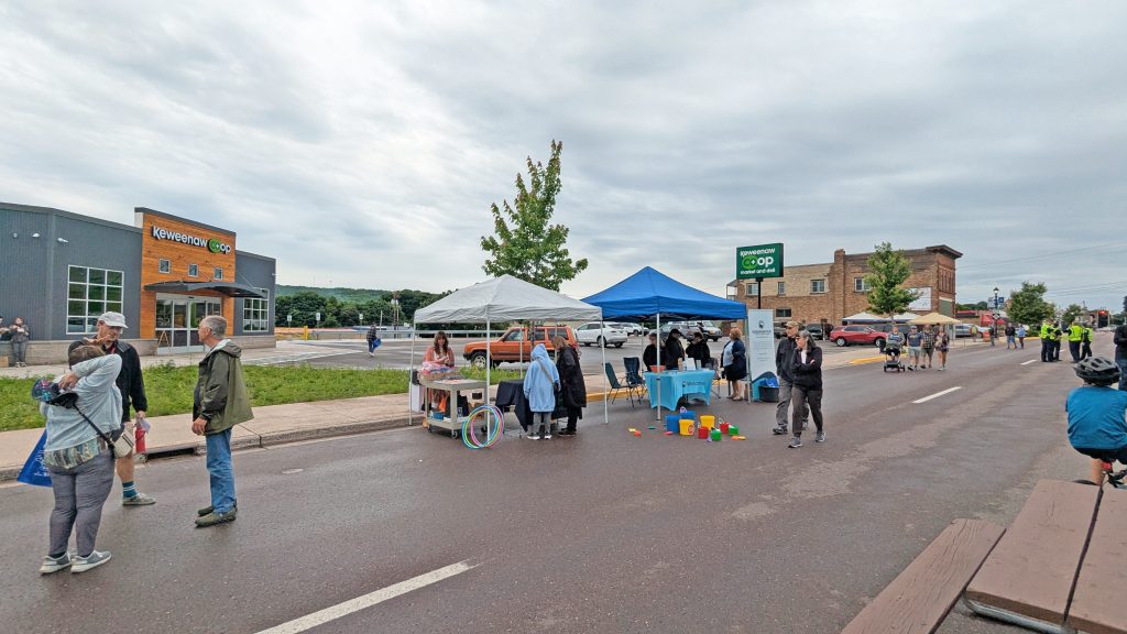 Photof two tents side by side for Keweenaw Co+op and Breakwater with people and giveaways at Key Ingredients.