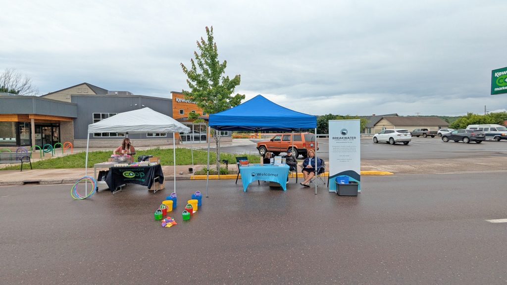 Photof two tents side by side for Keweenaw Co+op and Breakwater with people and giveaways at Key Ingredients.