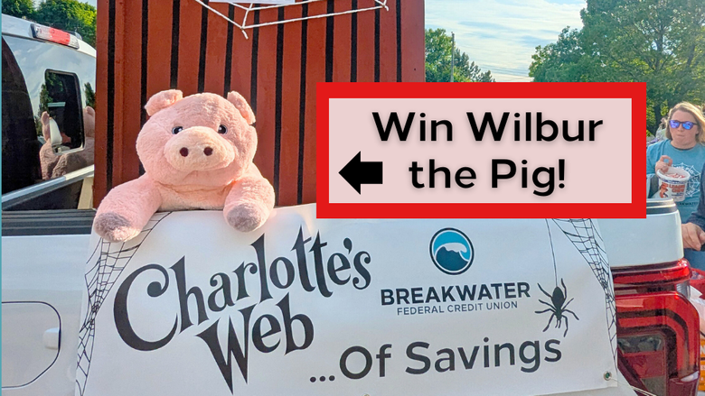 Photo of parade float. Banner says "Charlotte's Web of Savings" with Breakwater logo. Wilbur the pig is hanging over the side of the truck, with a large barn shaped structure covered in spider web behind him. Text on photo says "Win Wilbur the Pig!" with an arrow pointing towards the stuffed pig.