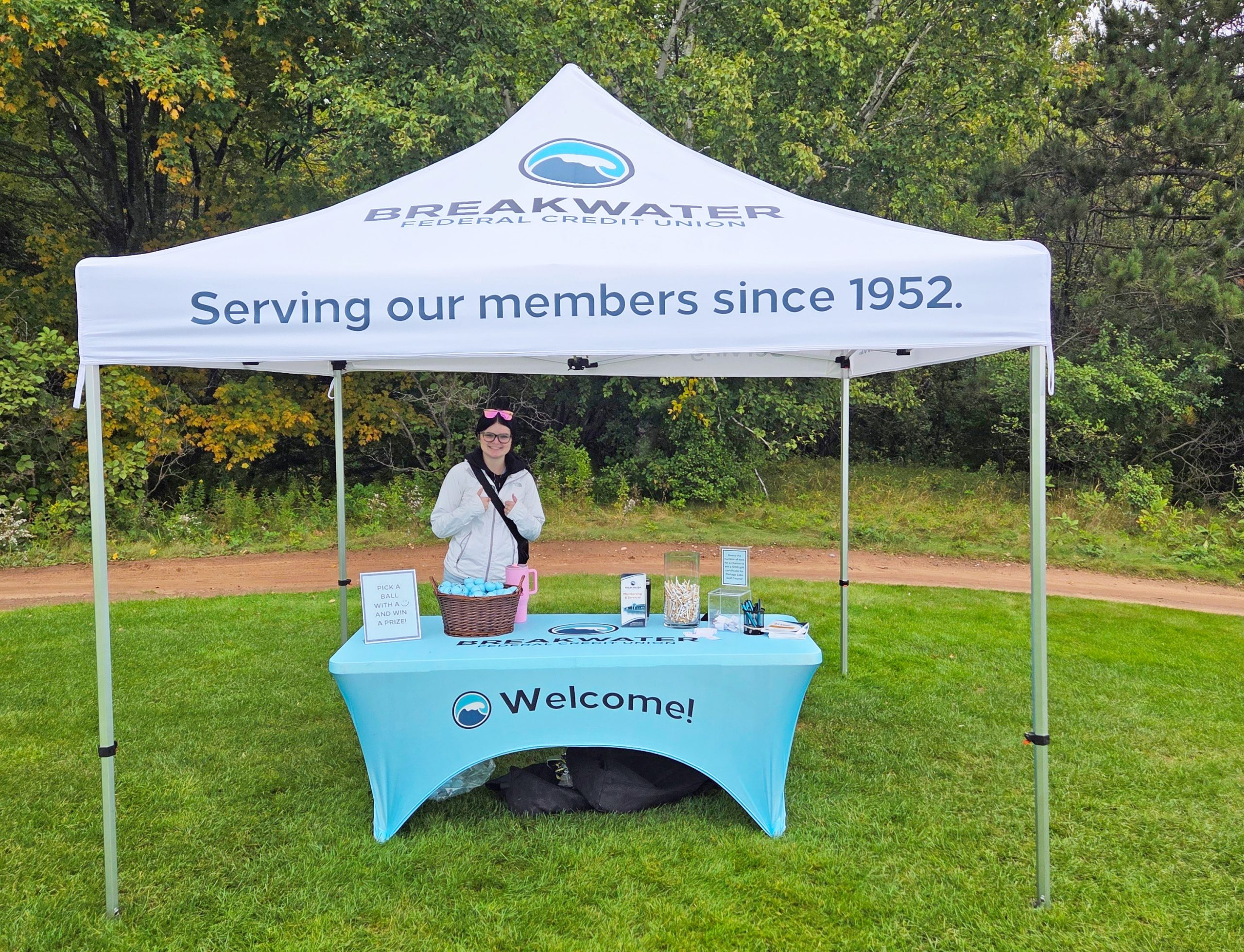 Breakwater employee smiles for photo at golf tournament booth, with golf balls and tees.