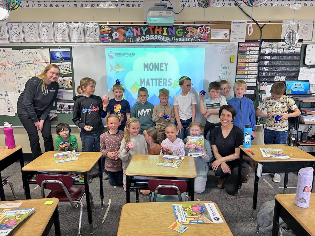 2nd grade students with piggy banks and Breakwater employees pose for picture.